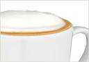 A close-up of a cappuccino in a white cup showing the frothy milk on top