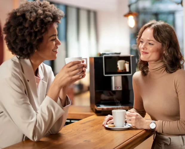 two women enjoying coffee at the office with solino coffee machine on the background