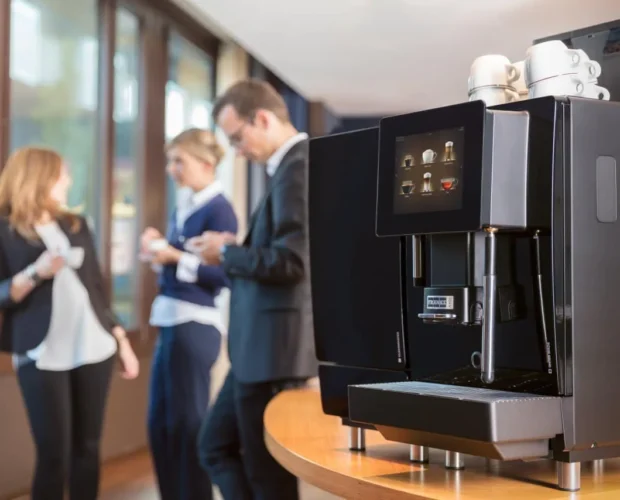 Franke fully automatic coffee machine in focus with a group of professionals engaged in conversation in the background.