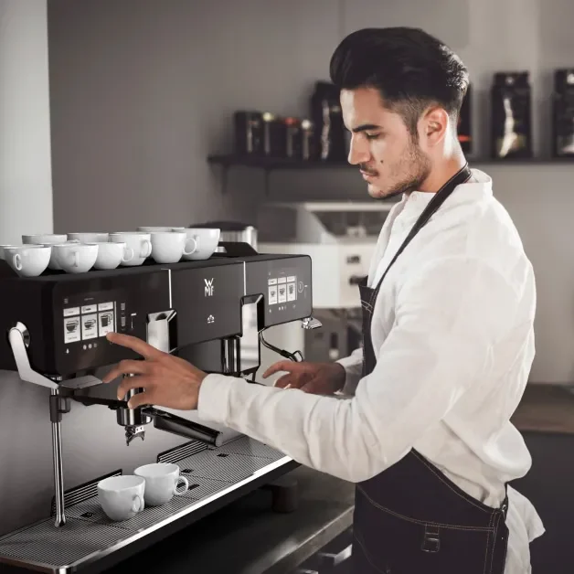 A barista attentively operates a WMF espresso NEXT professional espresso machine, preparing coffee in a café setting.